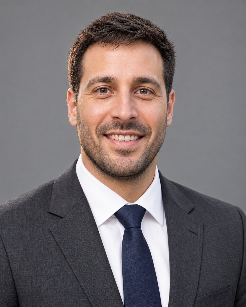 The same man in a suit and tie against a grey studio backdrop, with skin retouched until it looks artificial