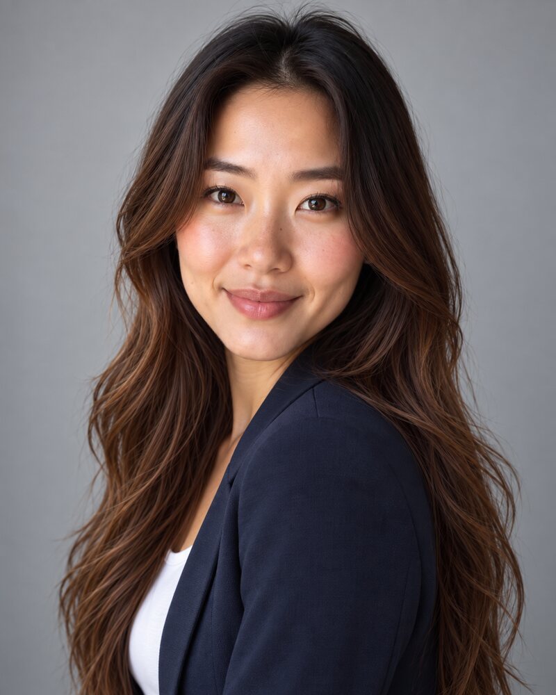 Woman in a navy blazer standing almost side-on and looking back at the camera over her front shoulder with a soft smile